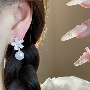 Elegant flower pearl earrings worn on an ear featuring pink blossom petals and zircon.