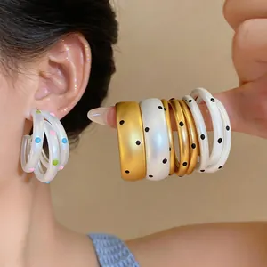 Detalle de pendientes de aro multicapa minimalistas con lunares en oro cepillado y blanco