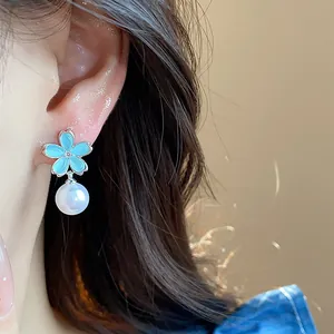 Macro view of an elegant blue flower and pearl earring worn on an Asian model's ear.