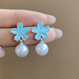 Detailed view of elegant light blue enamel flower stud earrings with white pearl drops