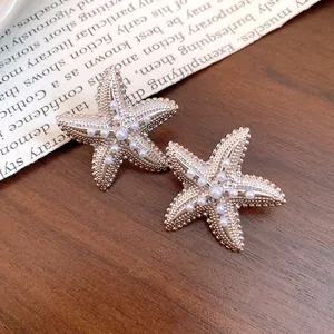 Primo piano dettagliato di eleganti orecchini a stella marina con perle bianche su legno