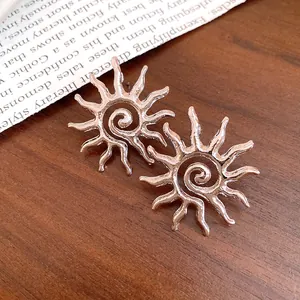 Dettaglio ravvicinato di orecchini a sole in argento con centro a spirale su legno.