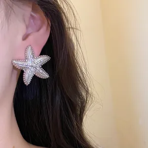 Primo piano di un grande orecchino a forma di stella marina argento con perle indossato da una modella.