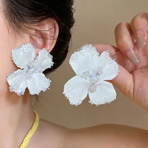 Primo piano di orecchini a fiore in tessuto bianco con bordi di perline e perla centrale