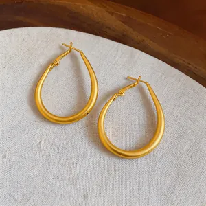 Primer plano de pendientes de aro dorados en forma de lágrima con elegante acabado mate