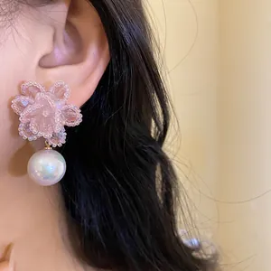 Dettaglio di orecchini a fiore in cristallo rosa con perla indossati da una modella