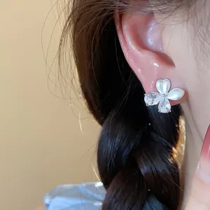 Détail rapproché de boucles d'oreilles fleur avec zircone et émail blanc sur l'oreille
