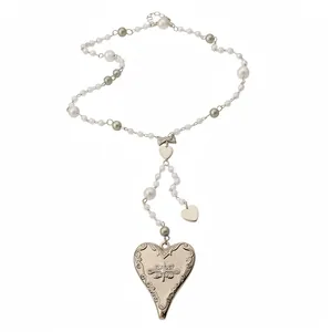 Vintage style heart pendant necklace with pearls and engraved metal details on white