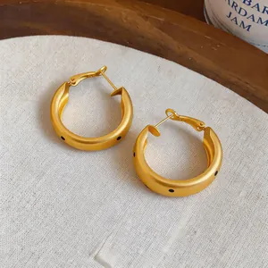 Detalle de pendientes de aro dorados cepillados con lunares negros sobre lino beige