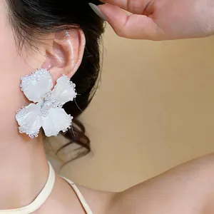 Primo piano di delicati orecchini a fiore in tessuto bianco con perle di vetro