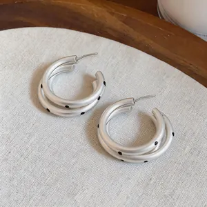Detalle de pendientes de aro plateados mate con lunares negros y diseño multicapa