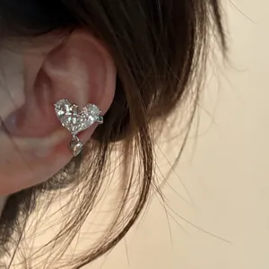 Gros plan d'un bijou d'oreille cœur argenté avec zircon brillant et croix ciselée