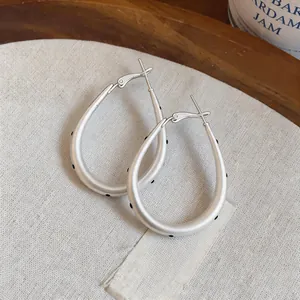 Detalle de pendientes de gota en plata mate con lunares negros y acabado cepillado