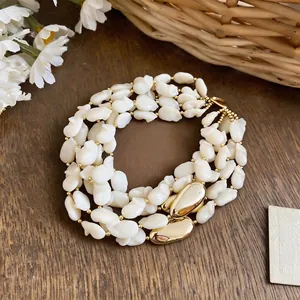 Élégant collier multicouche en perles de coquillage blanc avec accents dorés chic.