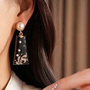 Vintage black enamel drop earrings with pearls and rhinestones on Asian model ear.