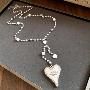 Close-up of elegant metal heart pendant and pearl beaded necklace on a display tray.