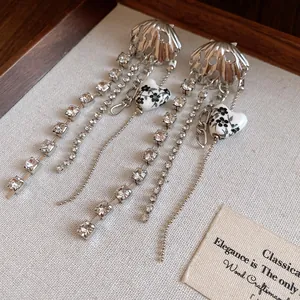 Close-up of elegant silver shell earrings with rhinestone tassels and floral hearts