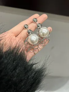 Detailed view of niche design metal chain and large pearl earrings shown in hand