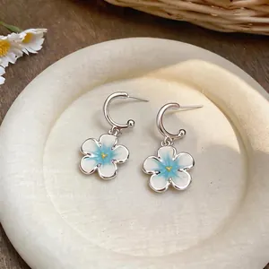 Dettaglio di orecchini a cerchio a forma di C con fiori smaltati bianchi e blu.