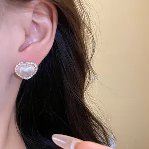 Close-up of an elegant heart-shaped pearl stud earring with a diamond-studded border on ear
