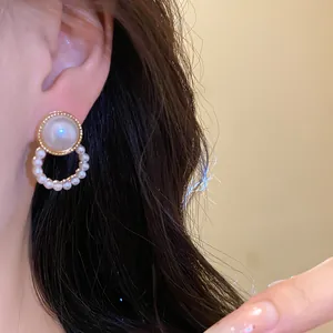 Close-up view of a gold rimmed pearl earring featuring a delicate hanging pearl circle