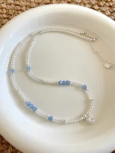 Close-up detail of beaded pearl necklace with blue crystals and clear stone pendant