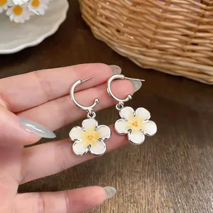 Vista ravvicinata di orecchini a cerchio in argento con fiori smaltati bianchi e gialli