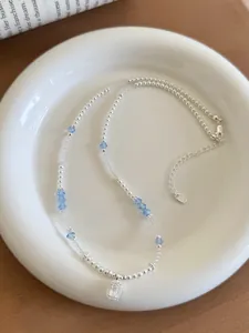 Close-up of elegant pearl beaded necklace with blue crystals and clear rectangular pendant.