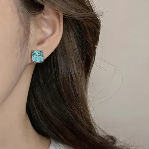 Detail view of a square-cut light blue zircon stud earring elegantly worn on model's ear