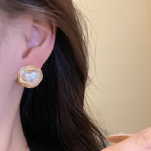 Detail shot of elegant heart pearl stud earrings with gold textured circular frame