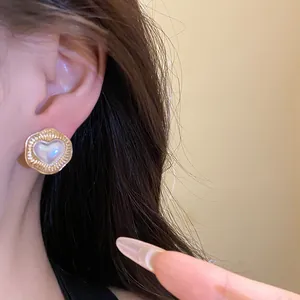 Detailed view of an elegant gold heart-shaped stud earring with a pearl center on ear.