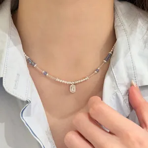 Close-up detail of a beaded pearl necklace with a rectangular crystal pendant on a model.