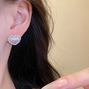 Close-up of elegant pearl heart stud earrings with sparkling diamond border on ear