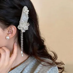 Close-up detail of an elegant French floral hair clip featuring white petals and long pearl tassels