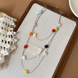 Detail shot of a minimalist colorful resin flower beaded necklace on a textured display tray.