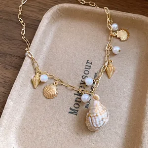 Dettaglio di una collana dorata stile vacanza con ciondoli a conchiglia e perle