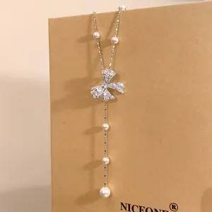 Gros plan d'un collier avec pendentif nœud serti de zircons et de perles blanches suspendues