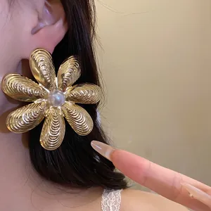 Grande orecchino a perno a fiore strutturato dorato con perla bianca indossato all'orecchio