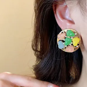 Elegant round stud earrings featuring colorful resin gourds and pearls worn by a model.