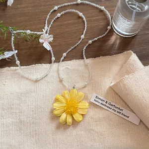 Detailansicht eines gelben Blumenanhängers an einer Perlen- und Glasperlenkette.