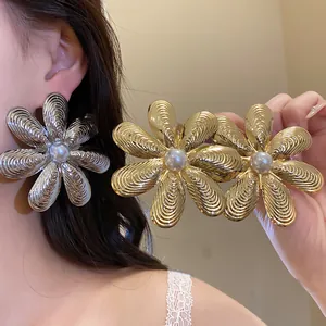 Dettaglio di grandi orecchini a fiore metallico con perla centrale e petali tramati