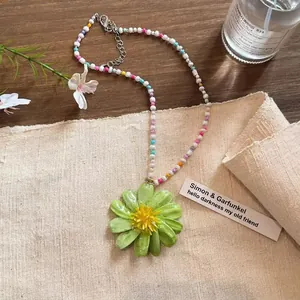 Detailansicht einer bunten Perlenhalskette mit einem großen grünen Blumenanhänger.