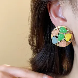 Close-up view of colorful resin and pearl round stud earrings worn on a female ear.