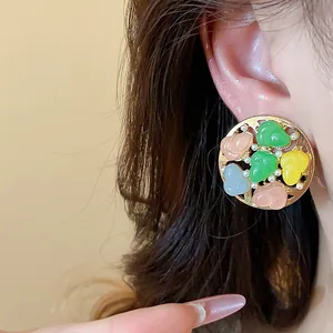 Close-up of a round stud earring with colorful resin stones and pearls on a model's ear