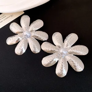 Dettaglio macro di orecchini a fiore color argento con petali testurizzati e perla centrale