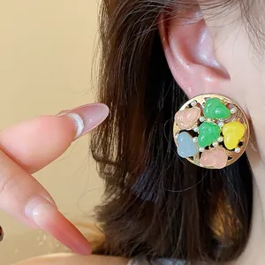 Macro shot of colorful resin round stud earrings with pearl accents worn on ear