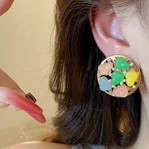 Close-up view of elegant round stud earrings featuring colorful resin hearts and small pearls.