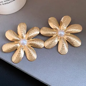 Dettaglio di orecchini a fiore in oro vintage con texture rigata e perla.