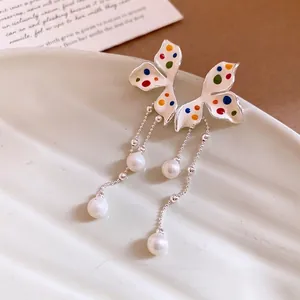 Orecchini a farfalla in smalto con nappe e perle su un piatto in ceramica minimalista
