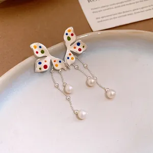 Dettaglio di eleganti orecchini a farfalla con pois colorati e nappe di perle bianche
